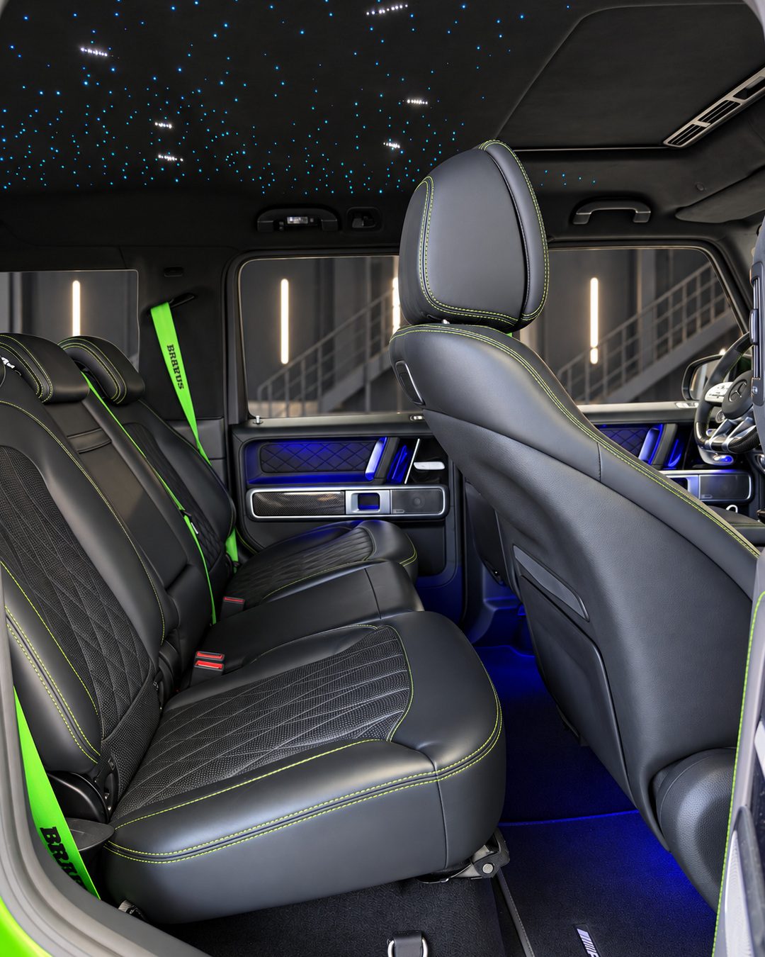 Mercedes-Benz G63 - Rear passenger area of the Mercedes-Benz G63 with black leather seats, contrasting green seat belts and illuminated interior trim.