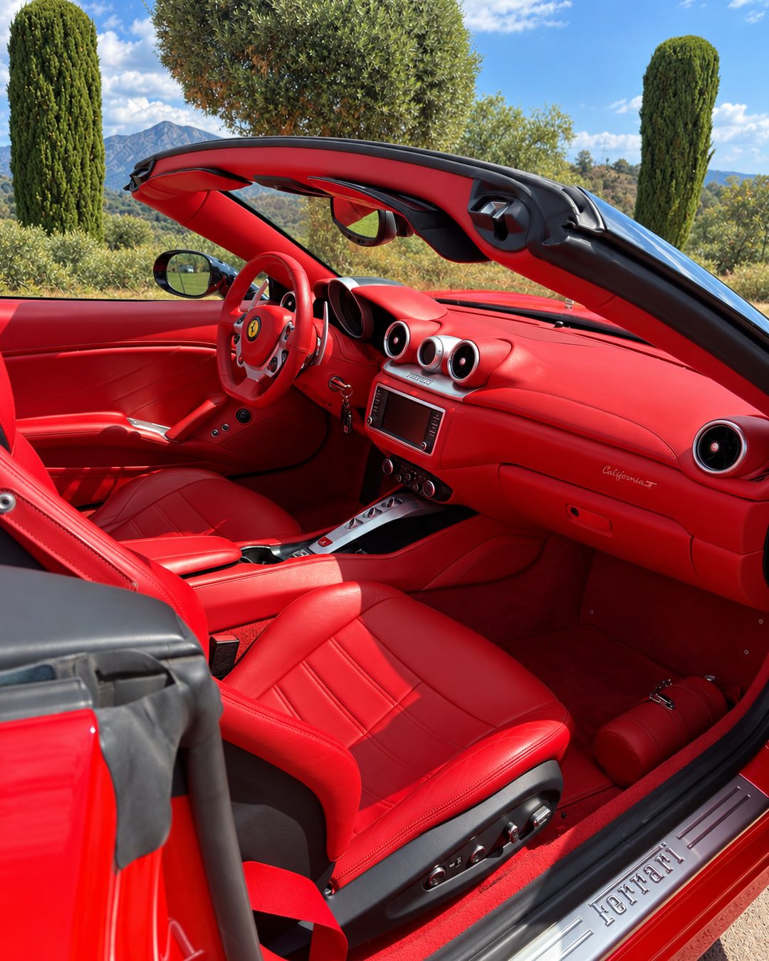 Водительское место Ferrari California T с красной кожаной приборной панелью, рулём Ferrari, центральными воздуховодами и мультимедийным экраном.