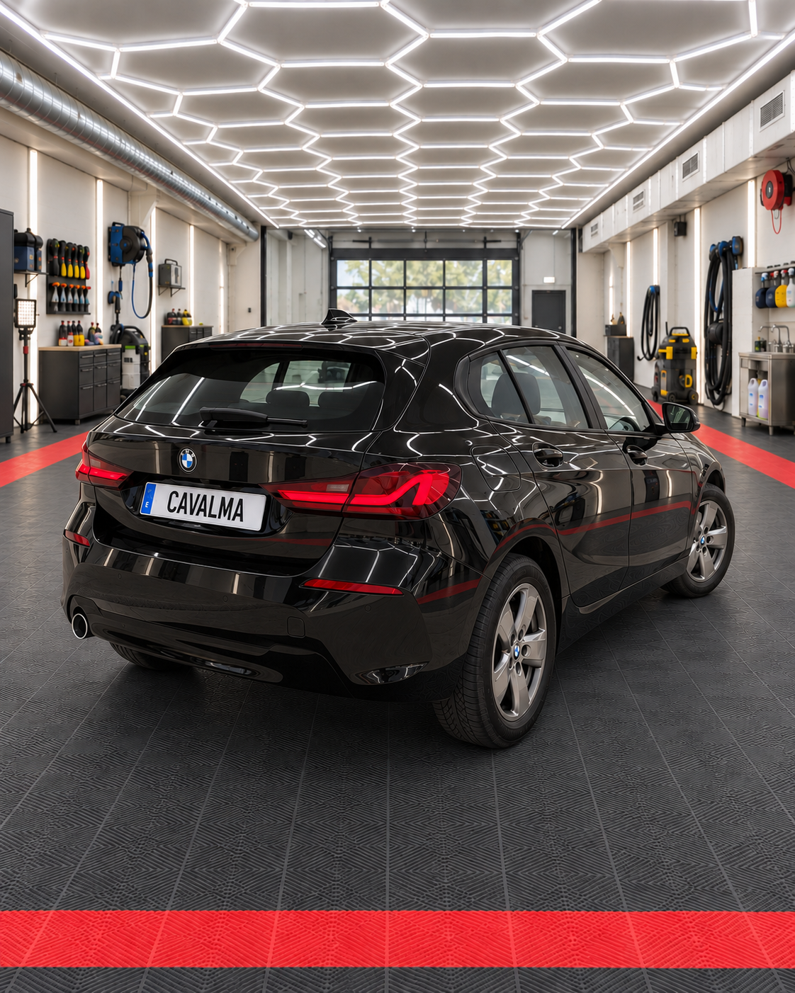Rear three-quarter view of a black BMW 1 Series hatchback inside the CAVALMA detailing facility, showing its rear lights, tailgate, rear bumper and alloy wheels.