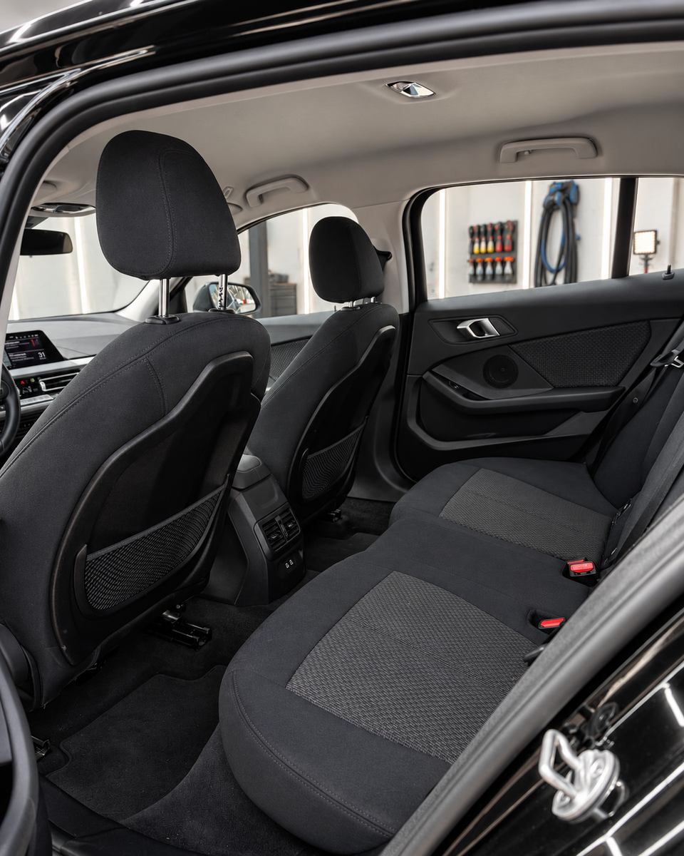 Rear passenger compartment of the BMW 1 Series with dark fabric seats, headrests, rear door trim and a view towards the front cabin.
