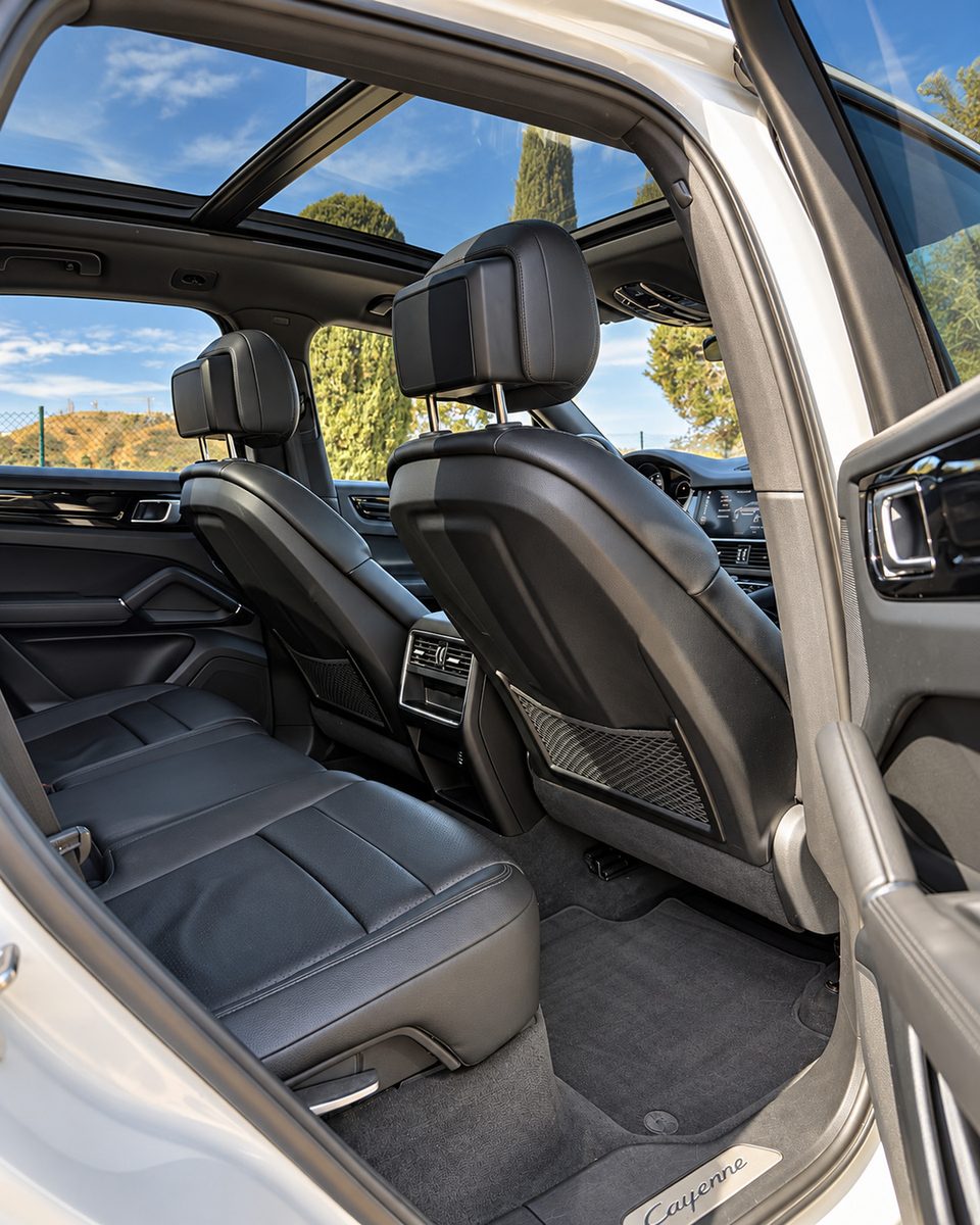 Porsche Cayenne rear passenger compartment with black seats, rear climate vents and panoramic glass roof.