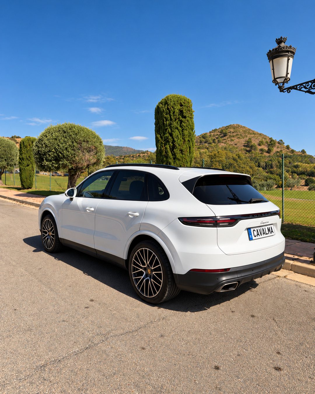 Porsche Cayenne بيضاء موديل 2020 بمنظر خلفي بزاوية ثلاثة أرباع، يظهر التصميم الجانبي والمصابيح الخلفية والجنوط المعدنية.